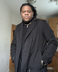 a man in a black coat standing in a kitchen